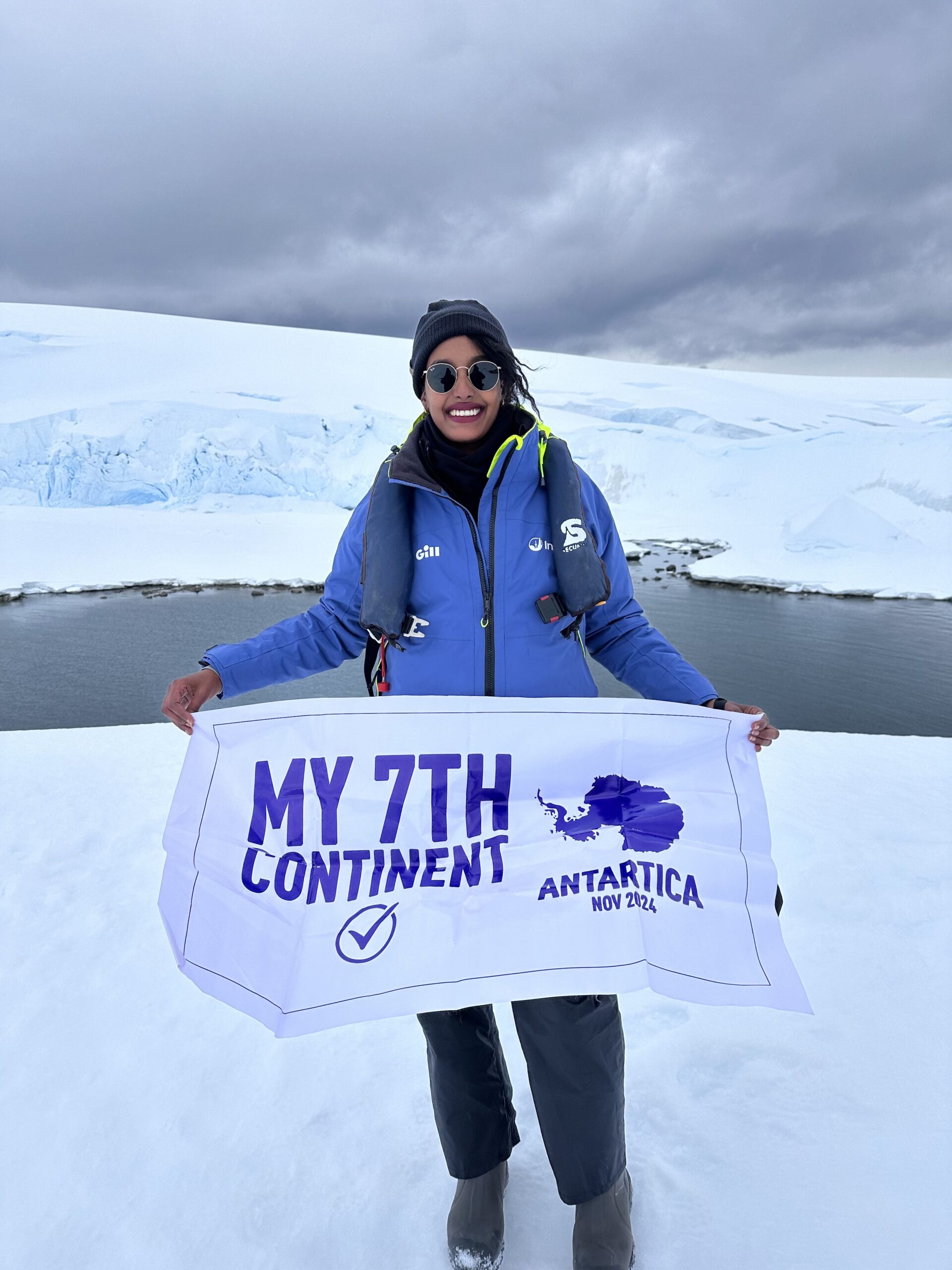 A Black woman traveling alone in Antarctica holding a flag that reads "My 7th Continent" during her solo journey.