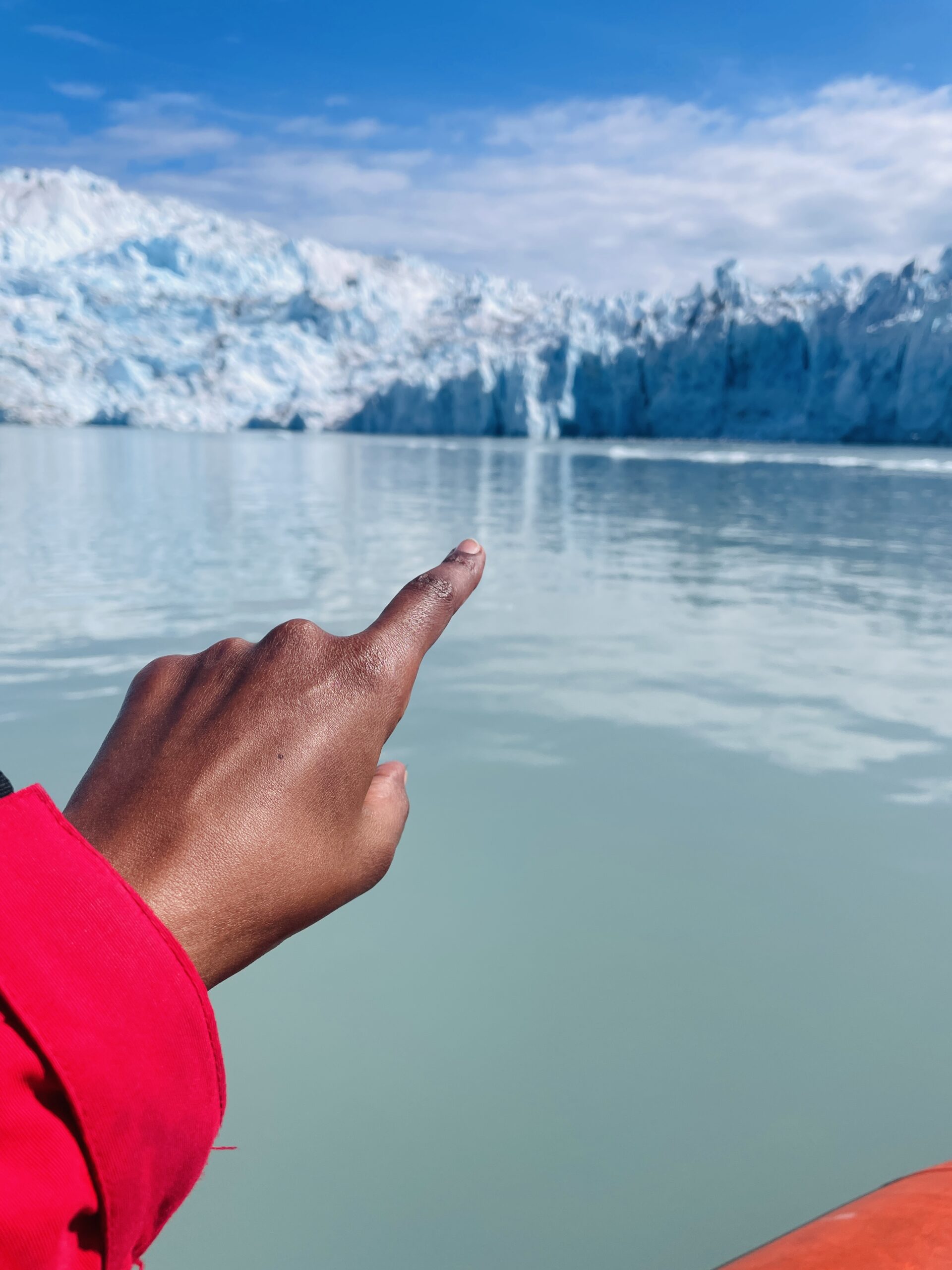 Solo traveler pointing at a massive iceberg in Greenland during Arctic adventure