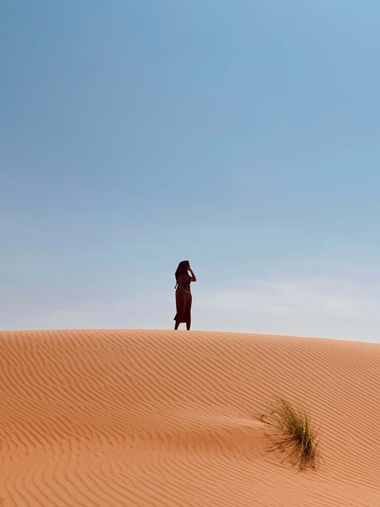 Solo female traveler exploring the desert alone in Oman, adventure travel in sand dunes