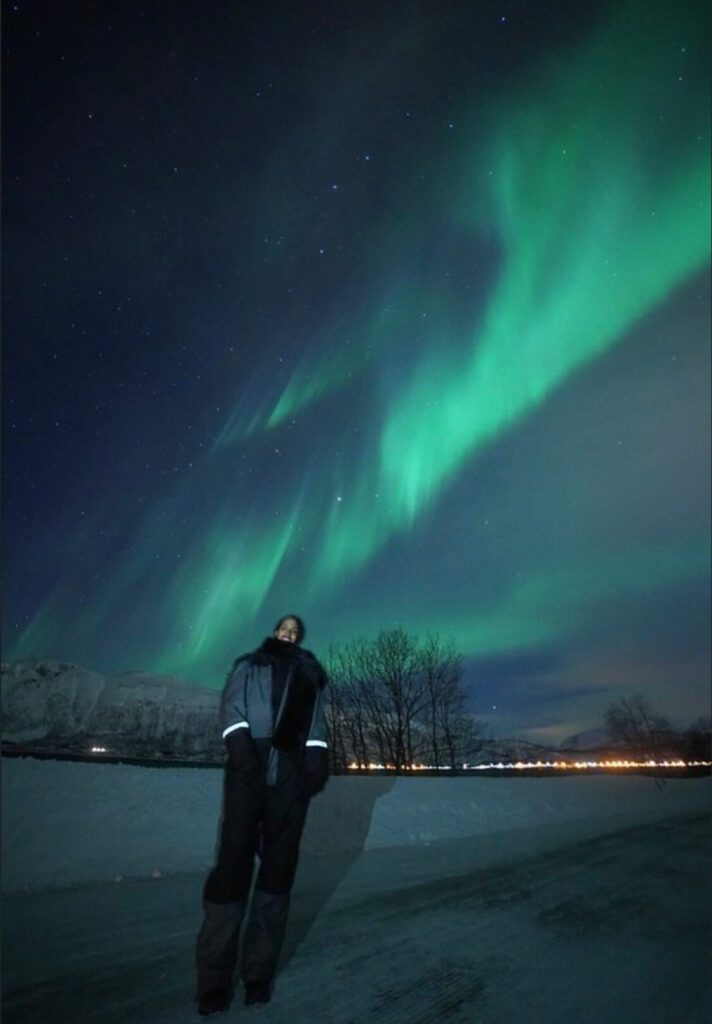 Solo female traveler in Norway watching the Northern Lights in winter landscape