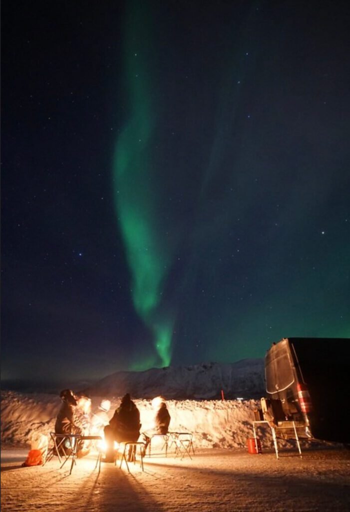 Solo female traveler sitting by a fire in the forest watching the northern lights in Norway