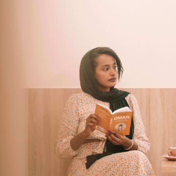 Solo female traveler in Oman enjoying coffee at a cozy café while reading a book