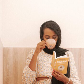 Solo female traveler in Oman enjoying coffee at a cozy café while reading a book