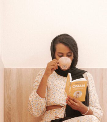 Solo female traveler in Oman enjoying coffee at a cozy café while reading a book