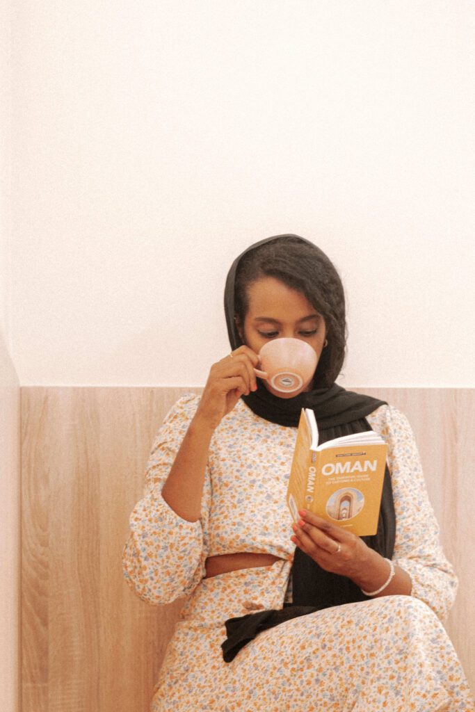 Solo female traveler in Oman enjoying coffee at a cozy café while reading a book