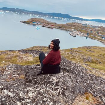 Female traveler enjoying a solo expedition in Greenland, walking across pristine snowy terrain in winter gear.