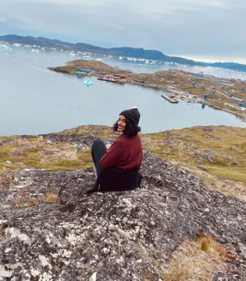 Female traveler enjoying a solo expedition in Greenland, walking across pristine snowy terrain in winter gear.