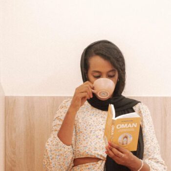 Solo female traveler working remotely on a laptop inside a café in Oman while enjoying a coffee