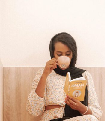 Solo female traveler working remotely on a laptop inside a café in Oman while enjoying a coffee