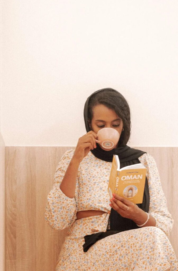 Solo female traveler working remotely on a laptop inside a café in Oman while enjoying a coffee