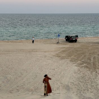 Solo female traveler sandboarding on sand dunes in Qatar, adventure travel in the desert