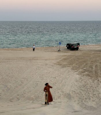 Solo female traveler sandboarding on sand dunes in Qatar, adventure travel in the desert