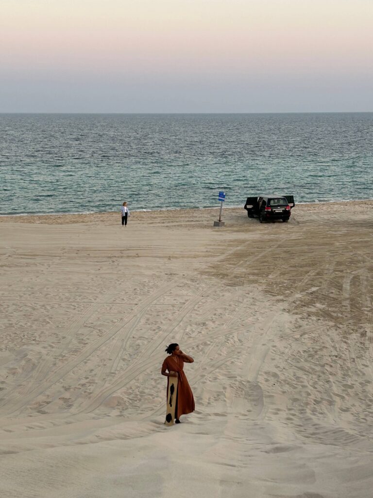 Solo female traveler sandboarding on sand dunes in Qatar, adventure travel in the desert