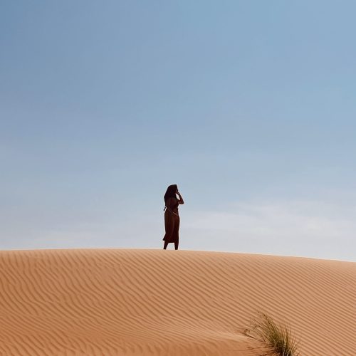 Female solo traveler in Oman desert standing on golden sand dunes during her solo trip