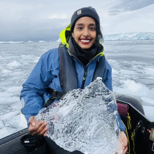 Solo female traveler exploring the icy landscapes of Antarctica, dressed in warm expedition gear, with glaciers and snow-covered terrain in the background.