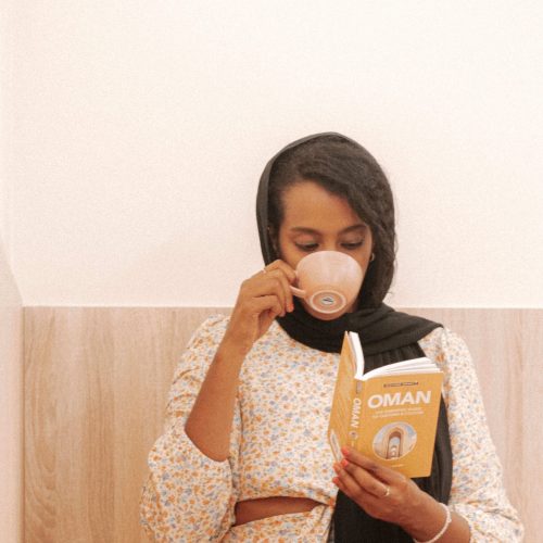 Solo female traveler in Oman enjoying coffee at a cozy café while reading a book